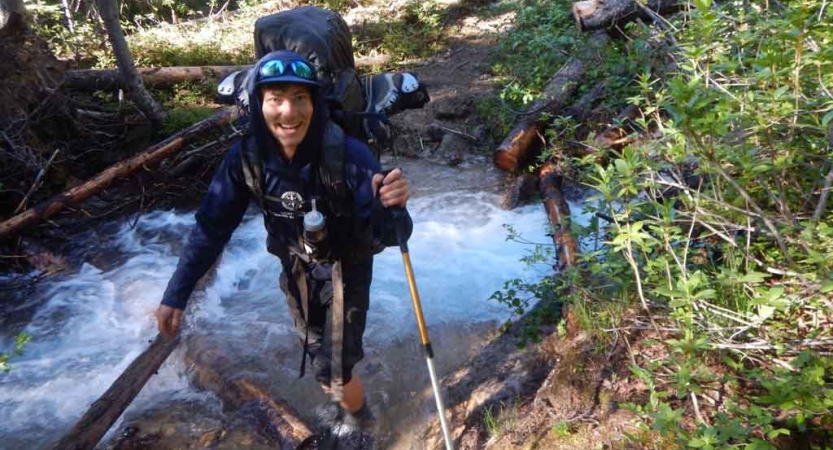 a person carrying a backpack crosses a creek on an outward bound course with outward bound